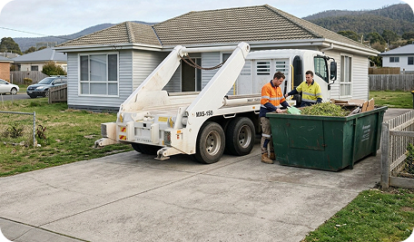 Skip Bin Hire Hobart operator collecting a filled skip bin containing green waste and household waste from a residential property in Bonnet Hill, Tasmania, demonstrating efficient on-site waste removal for garden, home, and renovation debris on a sloped coastal block