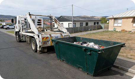 Skip Bin Hire Hobart truck collecting a full skip bin filled with household and rural waste in Grove, Tasmania, preparing to transport it to a licensed waste facility for disposal, showing efficient farm and home clean-up service on a rural property
